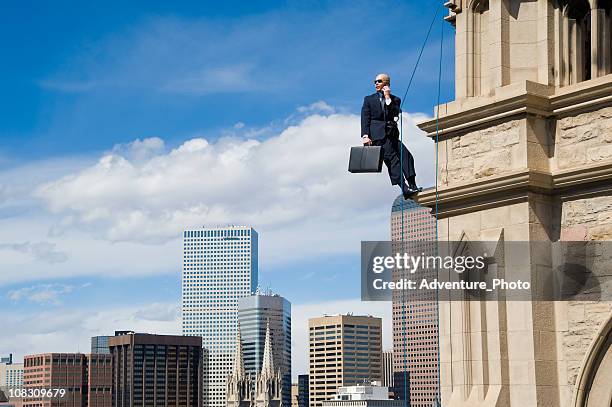 business man on rope in suit hanging off building - co op city stock pictures, royalty-free photos & images