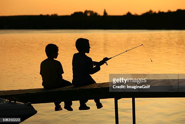 silhouette of two boys fishing off a dock - kids fishing stock pictures, royalty-free photos & images
