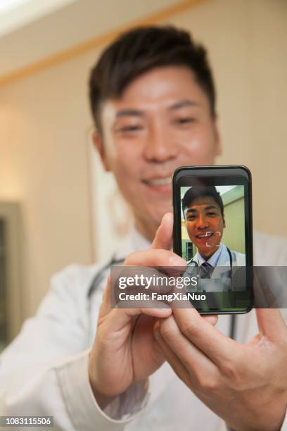 chinese doctor taking picture of himself with cell phone - doctor selfie stock pictures, royalty-free photos & images