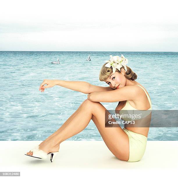 vintage pin-up girl sitting in front of a sea background - vintage pin up girl stock pictures, royalty-free photos & images