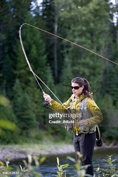 woman in yellow jacket casting a fly rod in lake - casting stock pictures, royalty-free photos & images