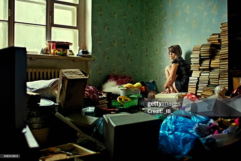 Lonely girl sitting in a room littered with things