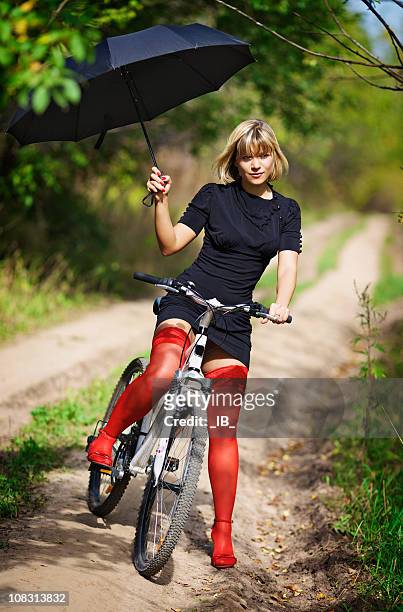 blonde in rot strümpfe auf einem fahrrad mit einem regenschirm - black stockings stock-fotos und bilder