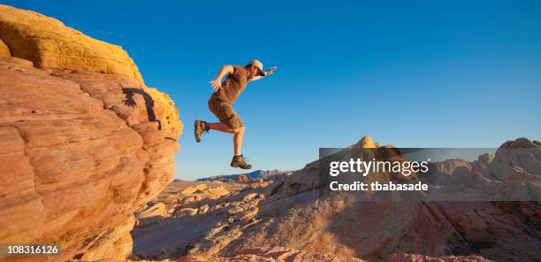 man takes leap of faith off of rock outcropping - nevada hiking stock pictures, royalty-free photos & images