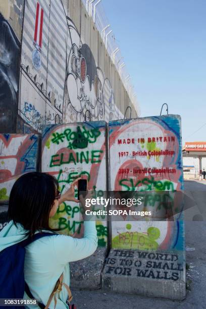 Tourist seen taking a picture of graffiti on the West Bank Separation Wall. The Israeli Separation Wall is a dividing barrier that separates the West...
