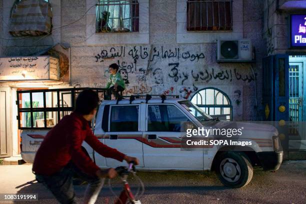 Kid seen seated on top a car parked on the street of the Dheisheh Refugee Camp with martyr graffiti in the background.