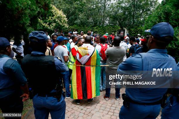 Members of the South African Police Services stand netx to protesters during a demonstration of Zimbabwean citizens outside the Zimbabwean Embassy in...