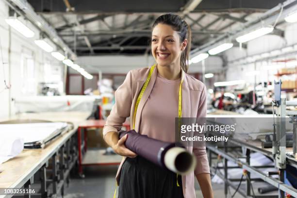 smiling young woman in a fashion factory - têxtil imagens e fotografias de stock