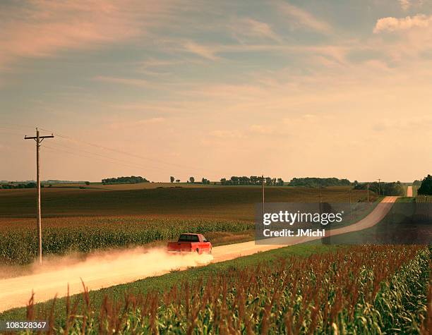 red pick up truck traveling down a dusty midwest road. - midwest stock pictures, royalty-free photos & images