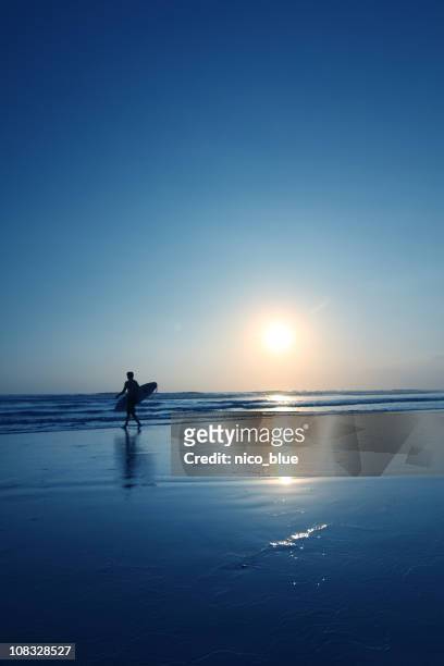 surfer bei sonnenuntergang - beach hold surfboard stock-fotos und bilder
