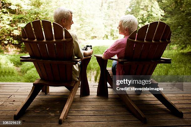 couple âgé se détendre dans les fauteuils adirondack sur une terrasse en bois - chaise adirondack photos et images de collection