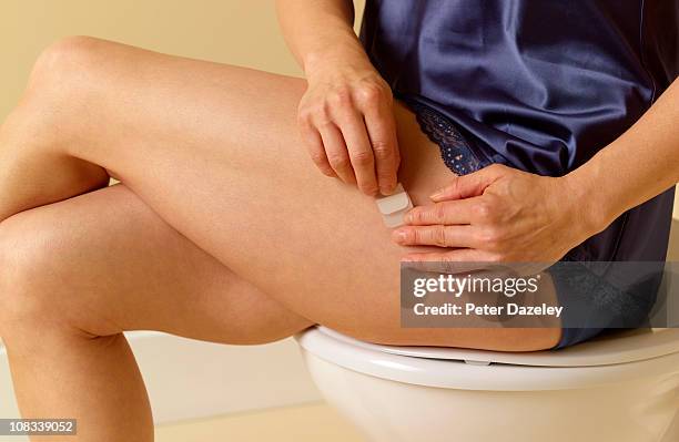 49 year old woman applying hrt patch to thigh - oestrogen stock pictures, royalty-free photos & images