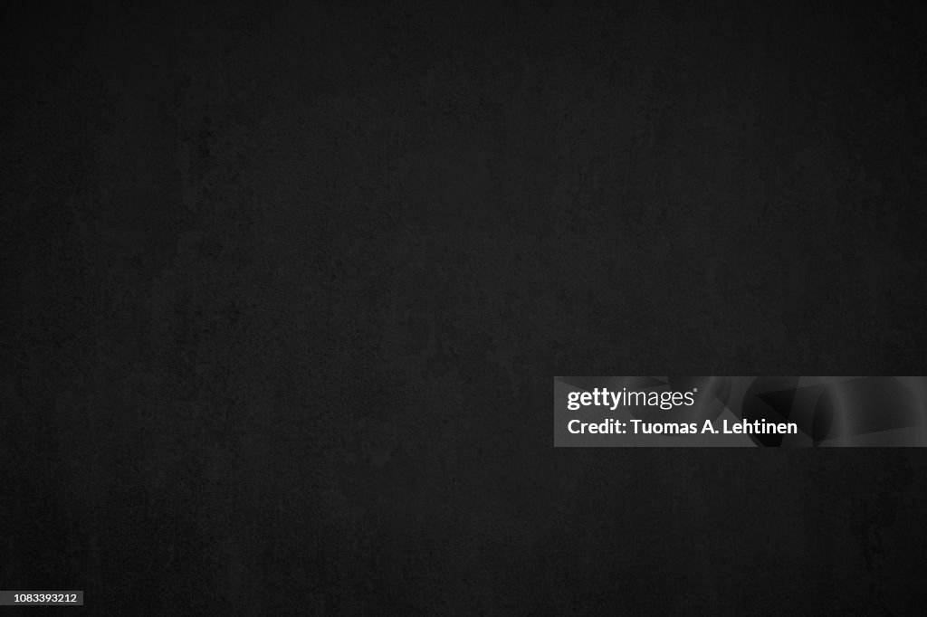 Close-up of a weathered and aged dark gray, almost black, concrete wall, texture background.