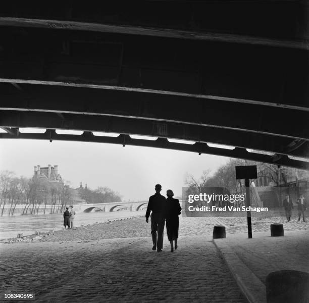 Courting couple walking under a bridge on the bank of the Seine, Paris, 1954.