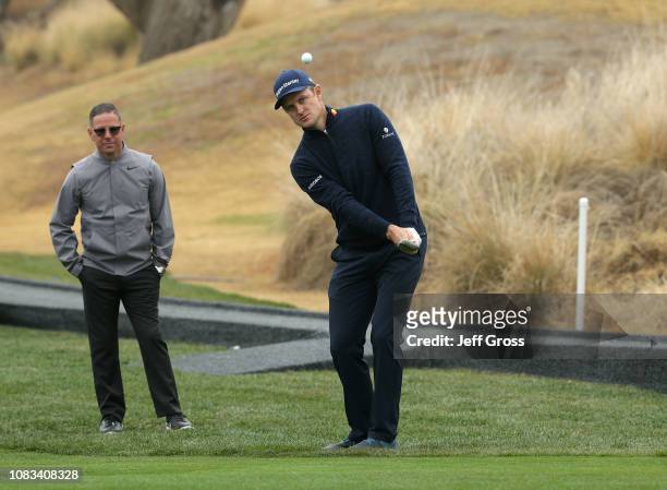 Justin Rose of England plays a shot, as swing coach Sean Foley looks on prior to the start of the Desert Classic at the Jack Nicklaus Tournament...