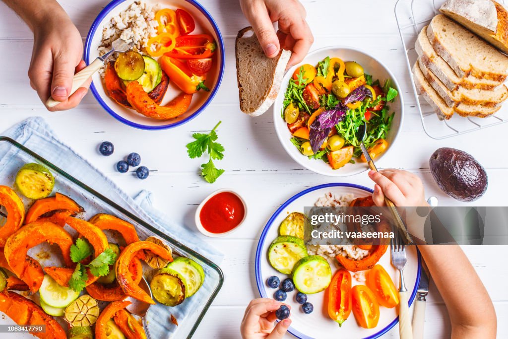 Family eating a healthy vegetarian food. Vegan lunch table top view, plant based diet. Baked vegetables, fresh salad, berries, bread on a white background.