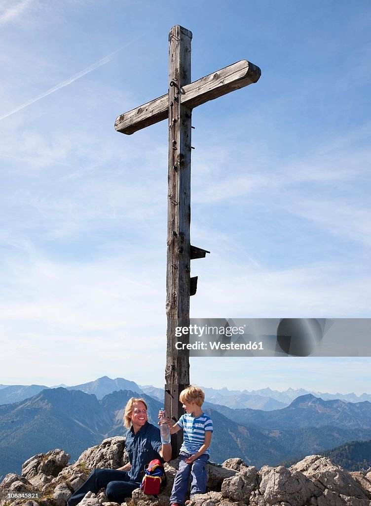Germany, Bavaria, Father and son (4-5 Years) sitting on mountain summit