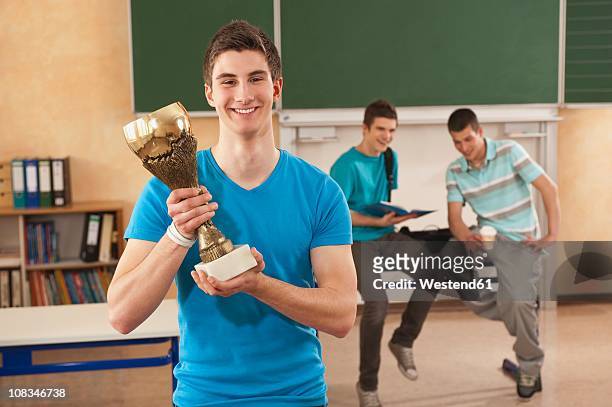 germany, emmering, young man holding trophy with students in background - holding trophy stockfoto's en -beelden