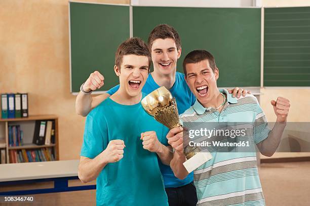 germany, emmering, friends holding trophy and clenching fist, smiling - teen awards - fotografias e filmes do acervo