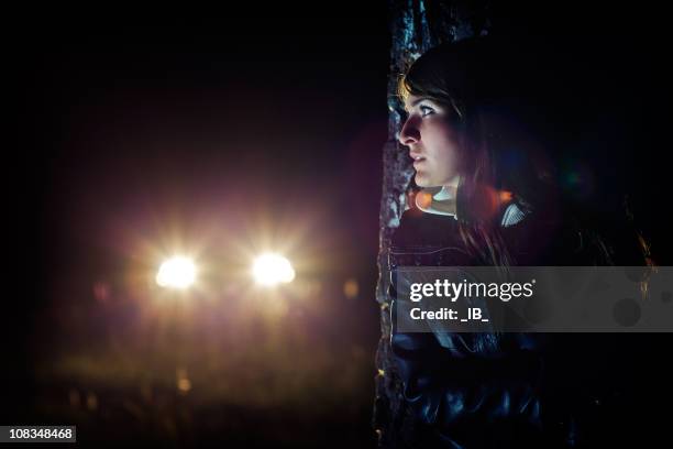 girl hides in the dark behind a tree from car - scared young woman in woods bildbanksfoton och bilder