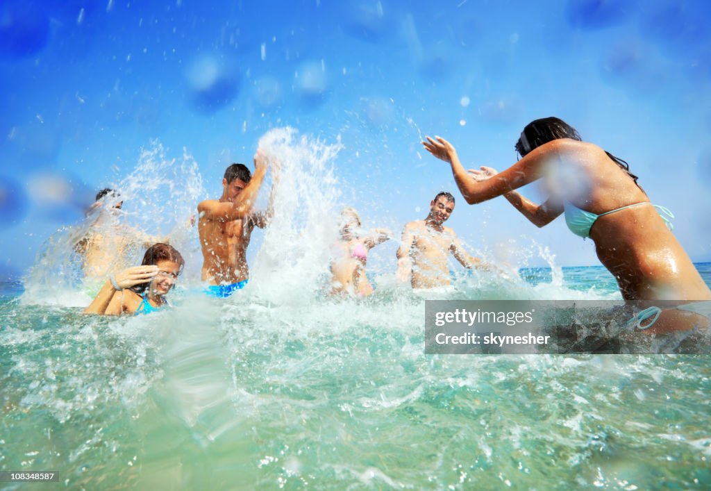 Young people in water spraying each other.
