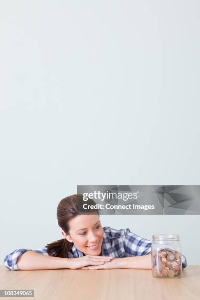 young woman with jar of coins - mano-en-la-barbilla fotografías e imágenes de stock