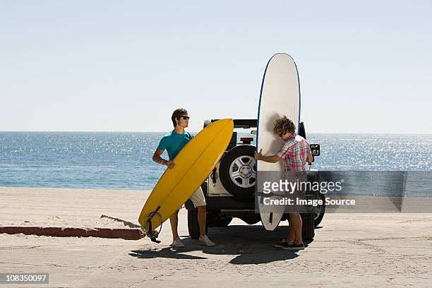 two young men by suv with surfboards - beach hold surfboard stock-fotos und bilder