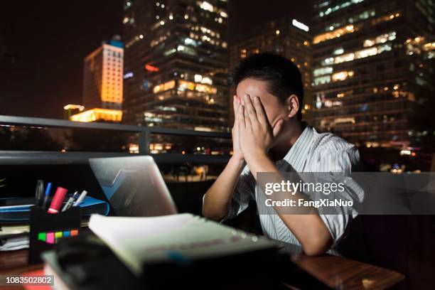 夜デスクで働く中国の実業家 - 手を顔にやる ストックフォトと画像
