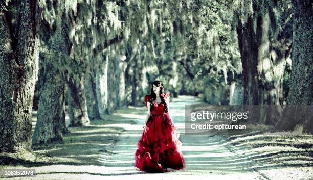 beautiful woman in red dress walking down white sand road - live oak tree stock pictures, royalty-free photos & images