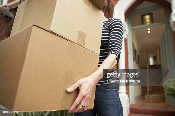 woman carrying brown boxes from house - carrying boxes stock pictures, royalty-free photos & images