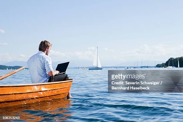 man sitting on a rowboat using laptob - starnberg photos et images de collection