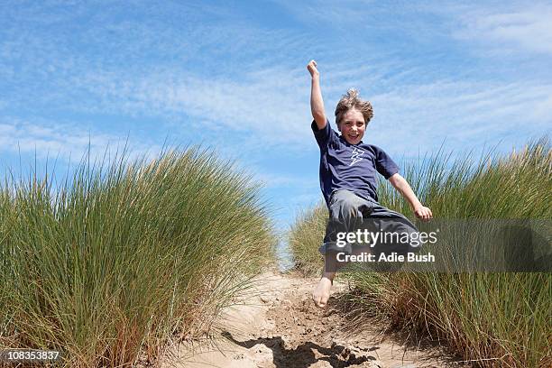 young boy jumping in sand dunes - sea grass stock pictures, royalty-free photos & images