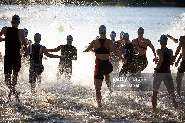 triathletes at start of triathlon running into the water. - triathlete stock pictures, royalty-free photos & images
