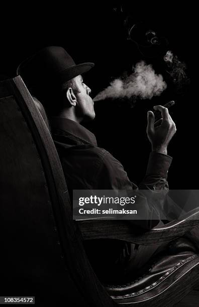 portrait of gang member sitting on armchair and smoking cigar - mob stock pictures, royalty-free photos & images