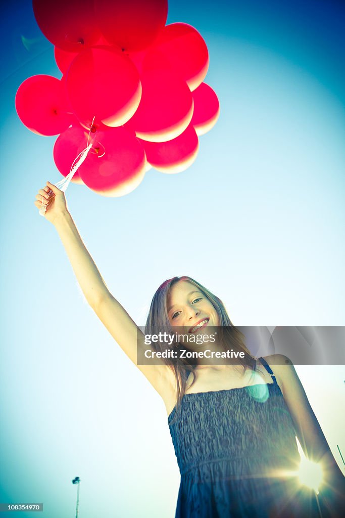 Toned beautiful young girl at sunny park with red baloons