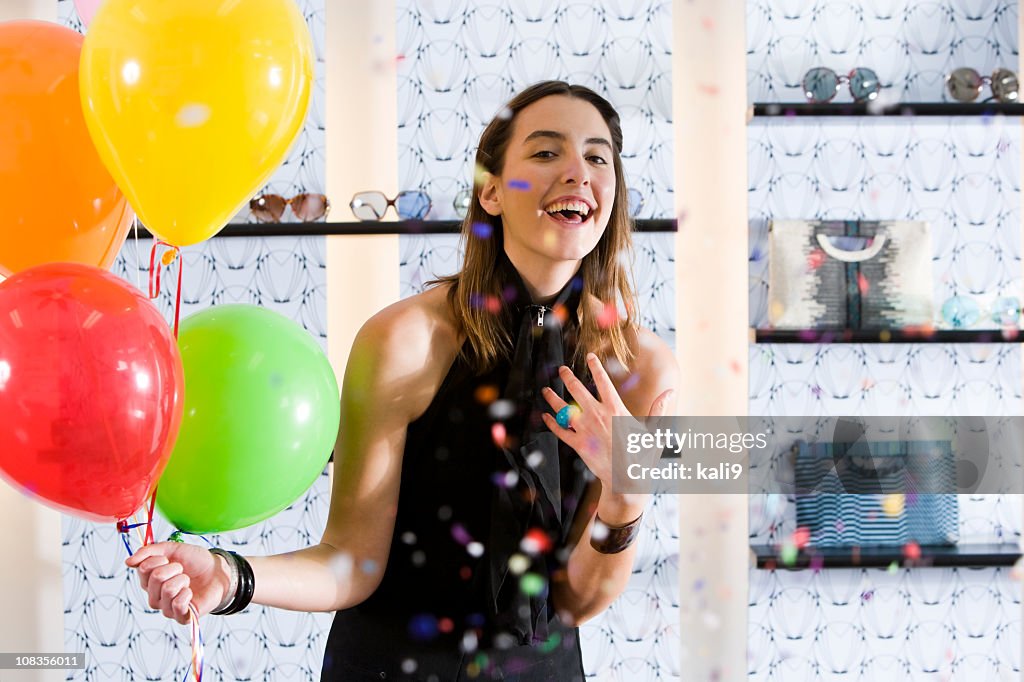 Happy young woman in boutique with balloons and confetti