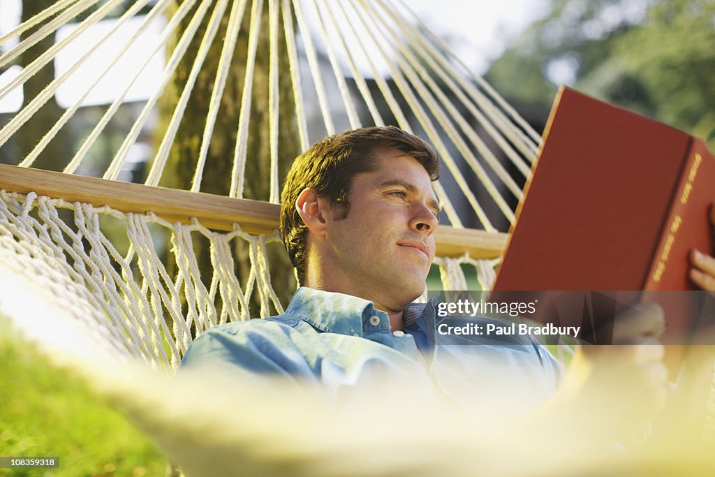 Mann liest ein Buch in der Hängematte Bauchlage