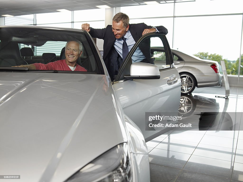 Salesman talking to man in new car in showroom