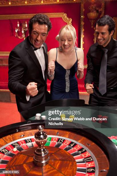 excited friends watching spinning roulette wheel - roulette stock pictures, royalty-free photos & images