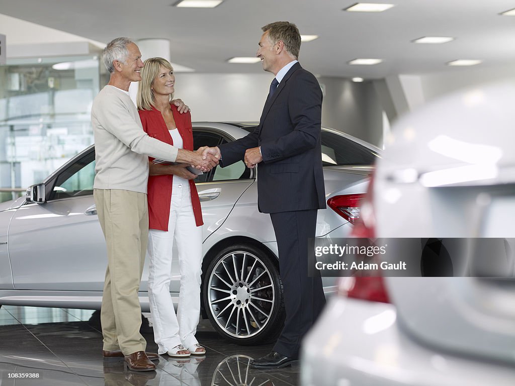 Salesman shaking hands with couple in automobile showroom