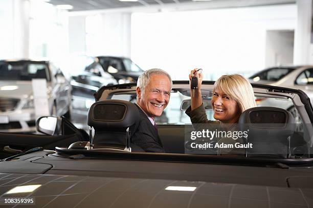 couple holding keys to new convertible in showroom - turning key stock pictures, royalty-free photos & images