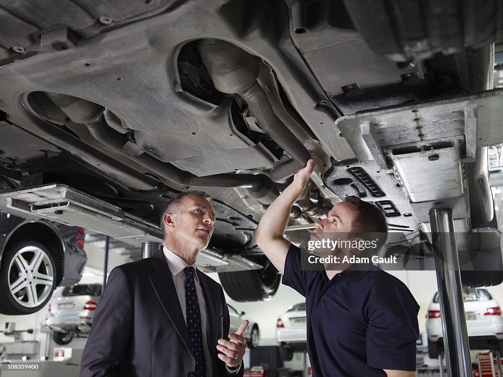 Businessman looking underneath car with mechanic