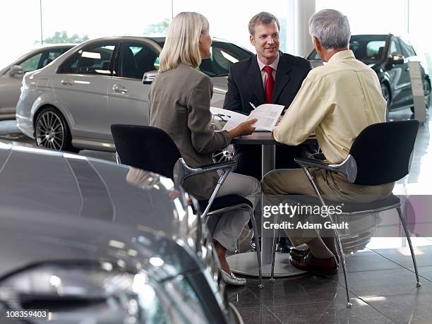 Salesman Talking To Couple In Automobile Showroom High-Res Stock Photo