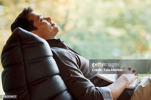 hombre dormir una siesta en las sillas reclinables en el sillón con libro - recostarse fotografías e imágenes de stock