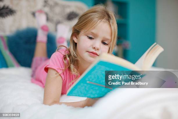girl laying on bed reading book - reading stockfoto's en -beelden