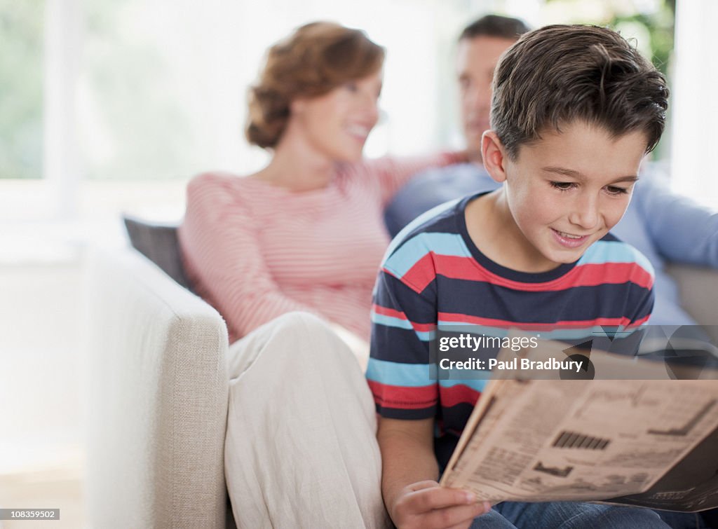 Petit garçon lisant journal avec les parents en arrière-plan