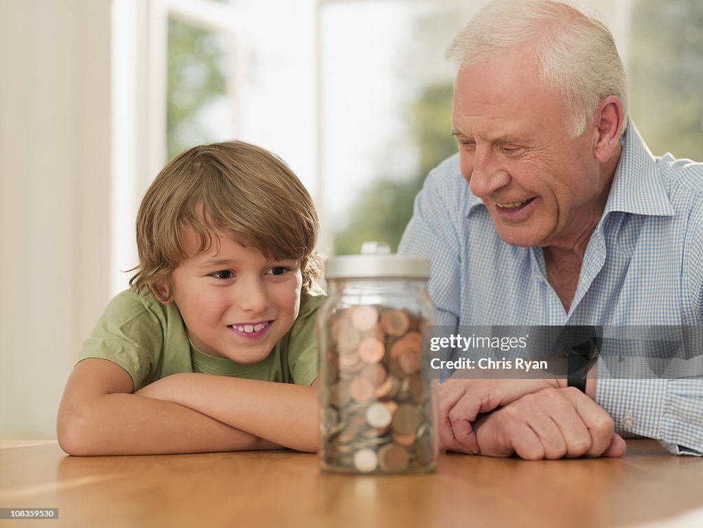 Grandfather and grandson looking at jar full of coins