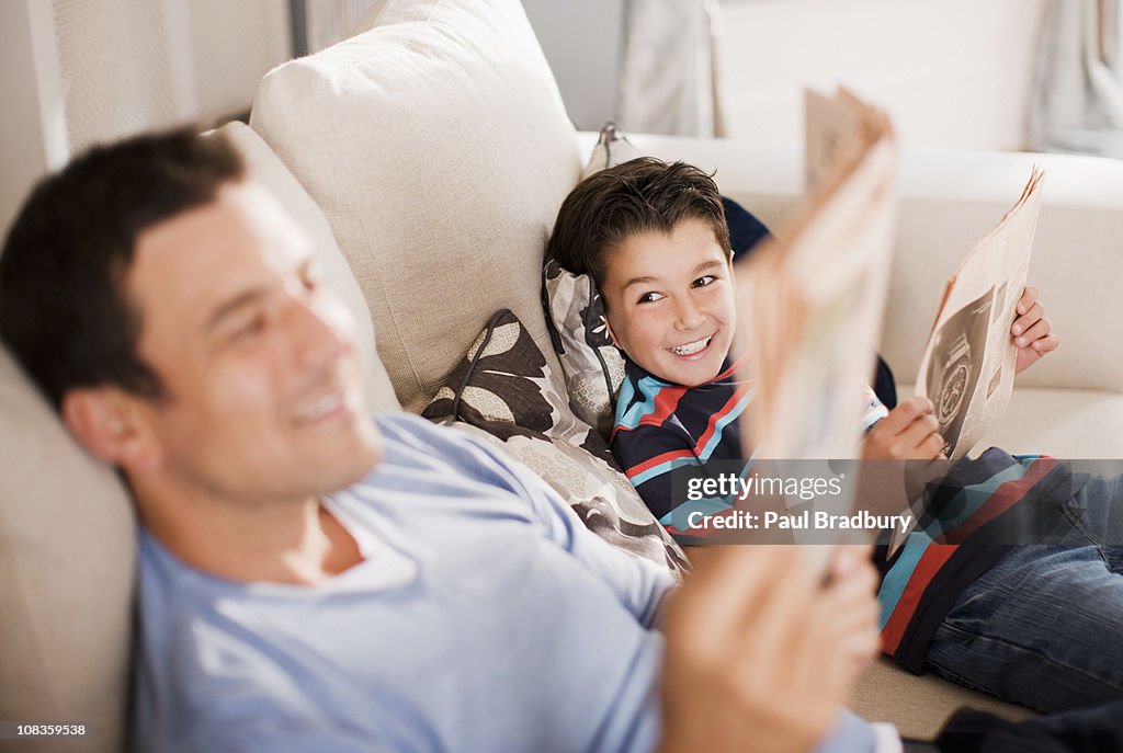 Father and son reading newspaper on sofa