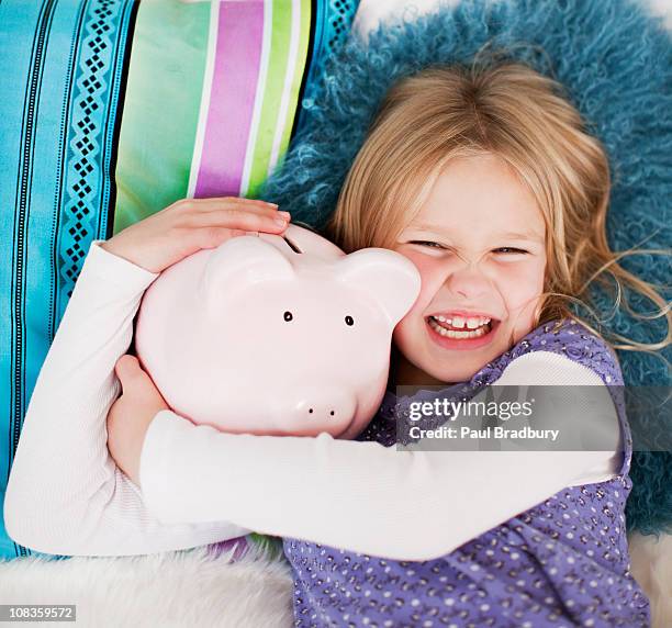 bauchlage grinsenden mädchen im bett mit sparschwein - blonde girl piggy bank stock-fotos und bilder