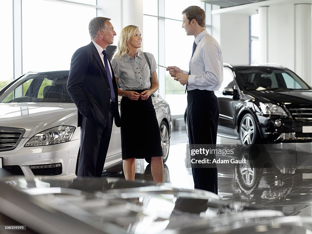 Salesman talking to couple in automobile showroom